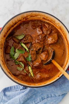 a pot filled with meat and vegetables on top of a table next to a blue towel