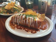 a burrito covered in sauce and cheese on a plate next to some potato chips