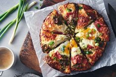 a pizza sitting on top of a wooden cutting board next to a cup of coffee