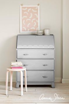 a grey dresser with books on it and a pink poster above the drawers in front of it