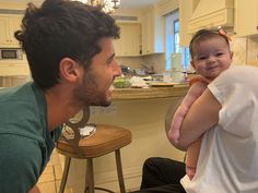 a man holding a baby in his arms while sitting next to a kitchen counter top