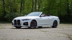 a white bmw convertible parked in front of some trees