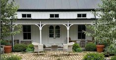 a white house with two chairs and a table in front of it on a brick patio