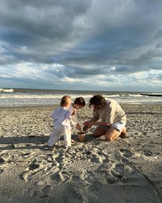 a man and two small children on the beach playing with sand in front of an ocean