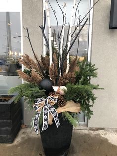 a large black vase filled with lots of greenery and christmas decorations in front of a building