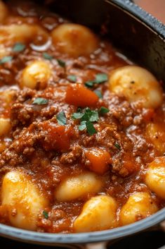 a pot filled with stew and potatoes on top of a wooden table next to a spoon