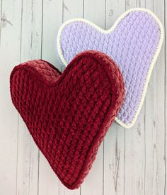 two crocheted heart shaped cushions sitting next to each other on a white wooden surface