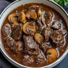 a white bowl filled with beef and mushrooms in gravy on top of a table