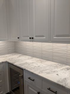 a kitchen with white cabinets and marble counter tops