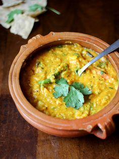 a wooden bowl filled with soup and garnished with cilantro, parsley and tortilla chips