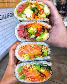 someone holding three sushi rolls with different types of vegetables and meats on them