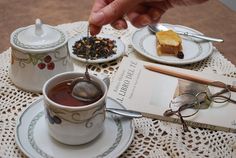 a table topped with plates and cups filled with tea next to books on top of a doily