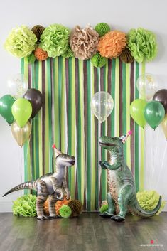 two dinosaur figurines sitting next to each other in front of balloons and streamers