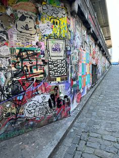 a wall covered in lots of graffiti next to a brick sidewalk with a person walking on it