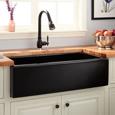 a black kitchen sink sitting under a faucet next to a bowl of fruit