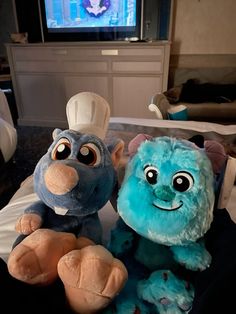 two stuffed animals sitting on top of a bed in front of a flat screen tv