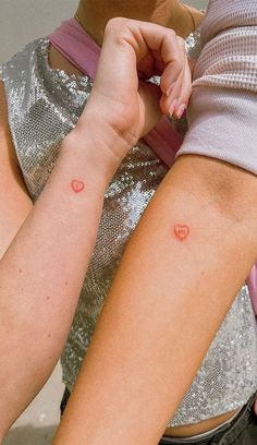 two women with tattoos on their arm and one has a small red dot in the middle