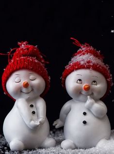 two snowmen standing next to each other with their noses covered in snow and wearing red hats