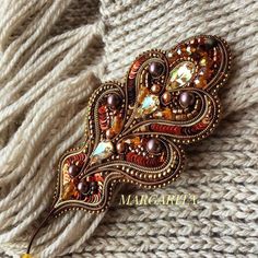 a close up of a brooch on a knitted surface with text that reads margartia