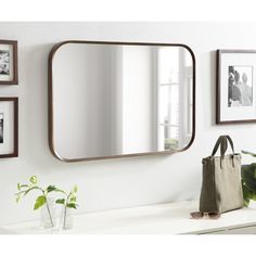 a mirror sitting on top of a white counter next to a vase and potted plant