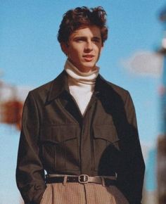 a man in a trench coat and turtle neck sweater standing on the street with his hands in his pockets