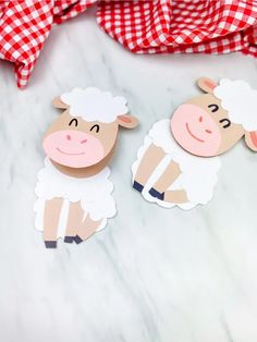 two sheep cutouts sitting next to each other on a marble counter top with red and white checkered fabric