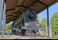 an old fashioned train is on display under a covered area with people standing next to it