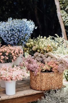 several different types of flowers in baskets on a wooden table with trees in the background