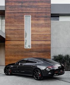 a black car is parked in front of a house with wood sidings on it