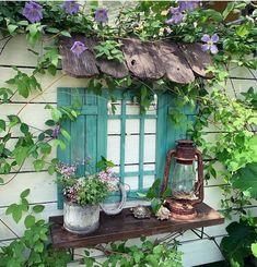 an old window with blue shutters and flowers growing on the outside, next to a potted plant