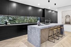 a modern kitchen with black cabinets and marble counter tops, along with bar stools