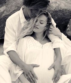 a pregnant woman sitting next to a man on top of a rocky beach with her head in her hands