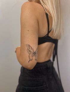 a woman with a butterfly tattoo on her arm and shoulder, standing in front of a white wall