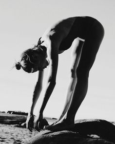 black and white photograph of a woman doing yoga on top of a rock at the beach