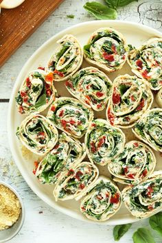 spinach rolls on a white plate with red peppers and seasoning next to them