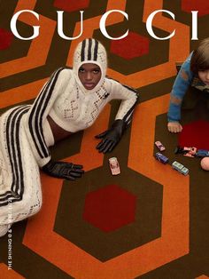 two children are sitting on the floor in front of a gucci advertisement for cell phones