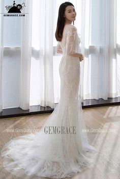 a woman standing in front of a window wearing a wedding dress with long sleeves and an open back