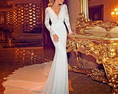 a woman standing in front of a mirror wearing a long sleeved wedding dress with sheer sleeves