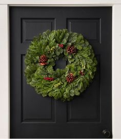 a christmas wreath hanging on the front door with pine cones and holly berries in it