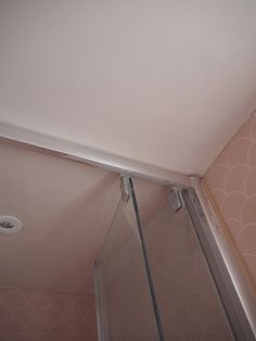 a bathroom with pink walls and white trim on the ceiling, along with a glass shower door