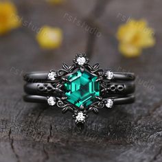 a ring with an emerald colored stone surrounded by white diamonds on a piece of wood