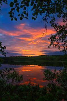 the sun is setting over a lake with trees around it and clouds in the sky