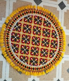 an intricately decorated plate on the floor with yellow tassels and red accents