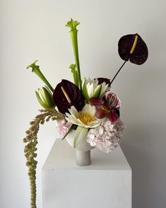 an arrangement of flowers in a vase on a white pedestal against a plain wall background