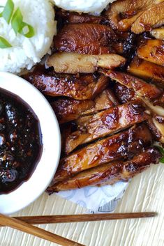 meat and rice on a plate with chopsticks next to the bowl filled with sauce