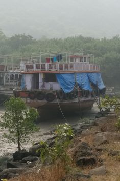 a large boat with blue tarps on it's sides in the water next to some rocks and trees