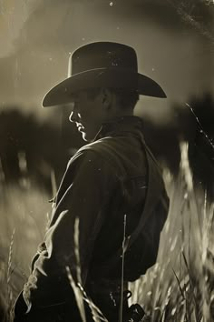 black and white photograph of a man wearing a hat in tall grass with his hands on his hips