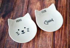 two white bowls with cat faces and words on them