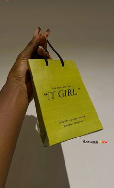 a hand holding a yellow shopping bag that says it's girl