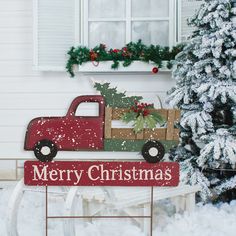 a red truck is parked next to a christmas tree in front of a white house